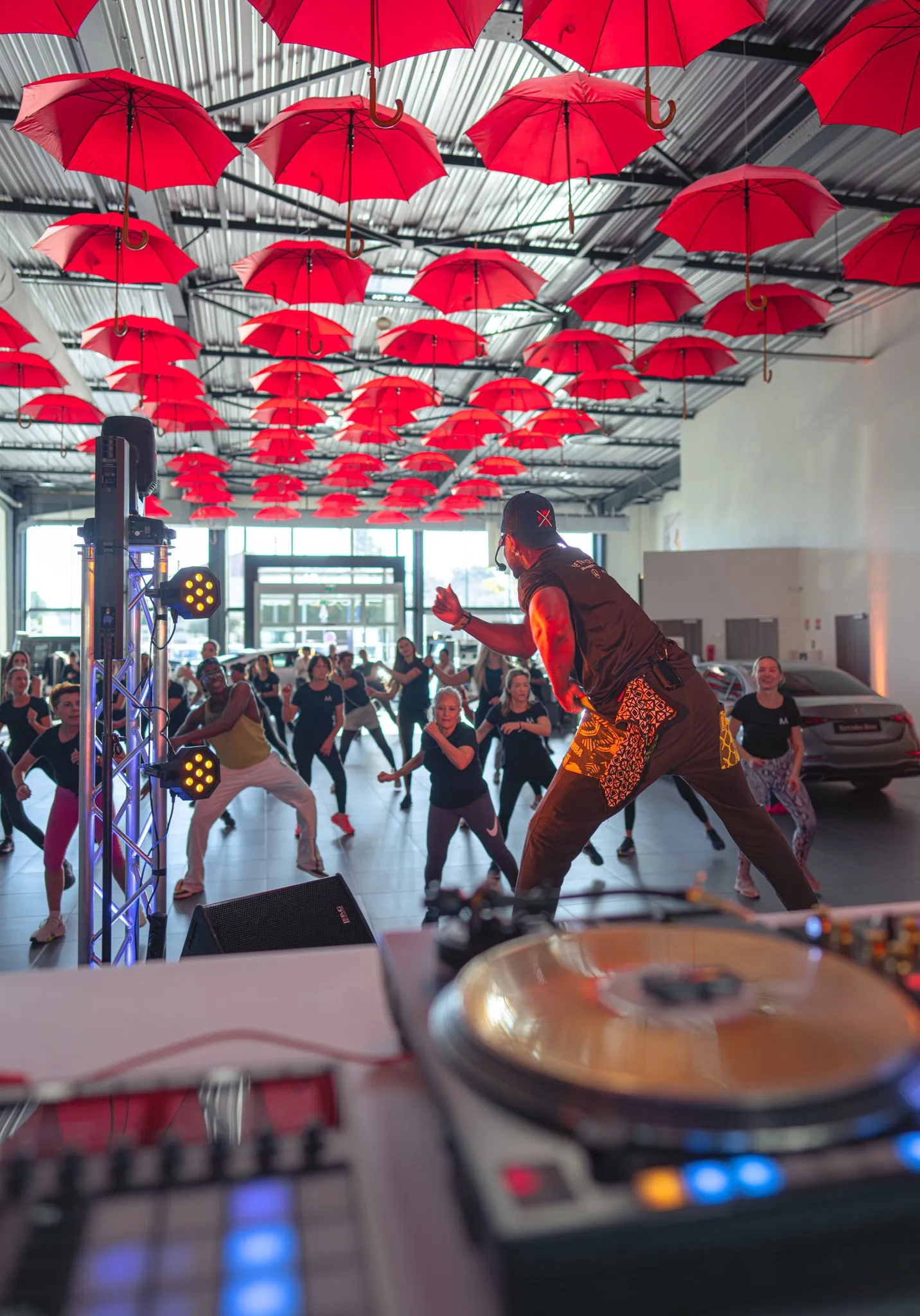 Cours collectif de Zumba dans une grande salle décorée de parasols rouges, platines DJ au premier plan