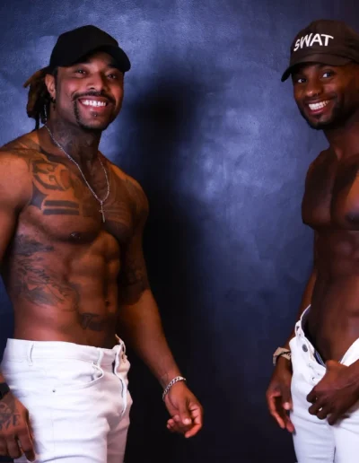 Deux gogo danseurs souriants en pantalon blanc et casquettes, photographie de studio
