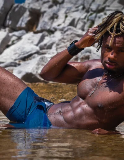 Danseur allongé dans l'eau au bord de rochers, en short bleu