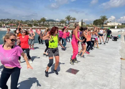 Cours de Zumba en plein air sur une esplanade face à la mer, nombreux participants en train de danser