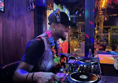 DJ aux platines lors d'une soirée, casque autour du cou et collier de fleurs, ambiance colorée