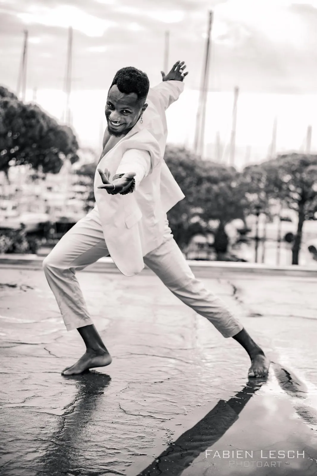 Danseur en costume blanc en pleine figure de danse sur un quai, devant un port, photographie en noir et blanc