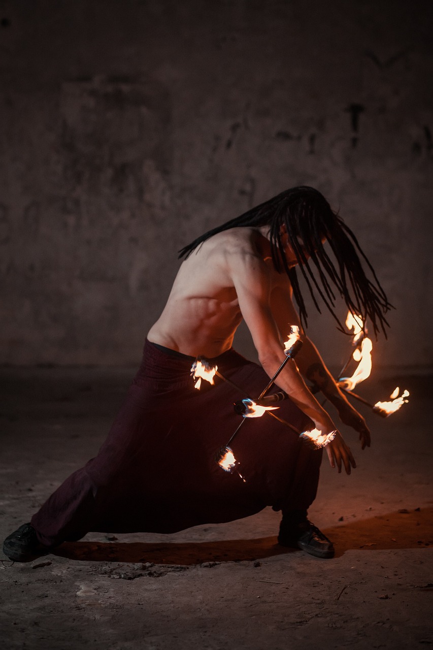 Performeur de feu torse nu, accroupi, manipulant des torches enflammées dans un décor sombre