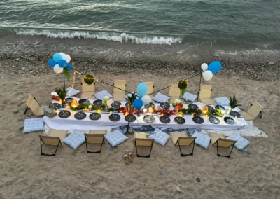 Vue aérienne d'une longue table basse dressée sur le sable, décoration bleu et blanc, au bord de l'eau