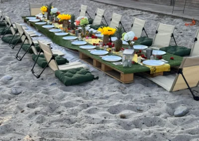 Dîner romantique pour deux sur les rochers, arche dorée drapée de voile rouge et guirlandes, face au soleil couchant