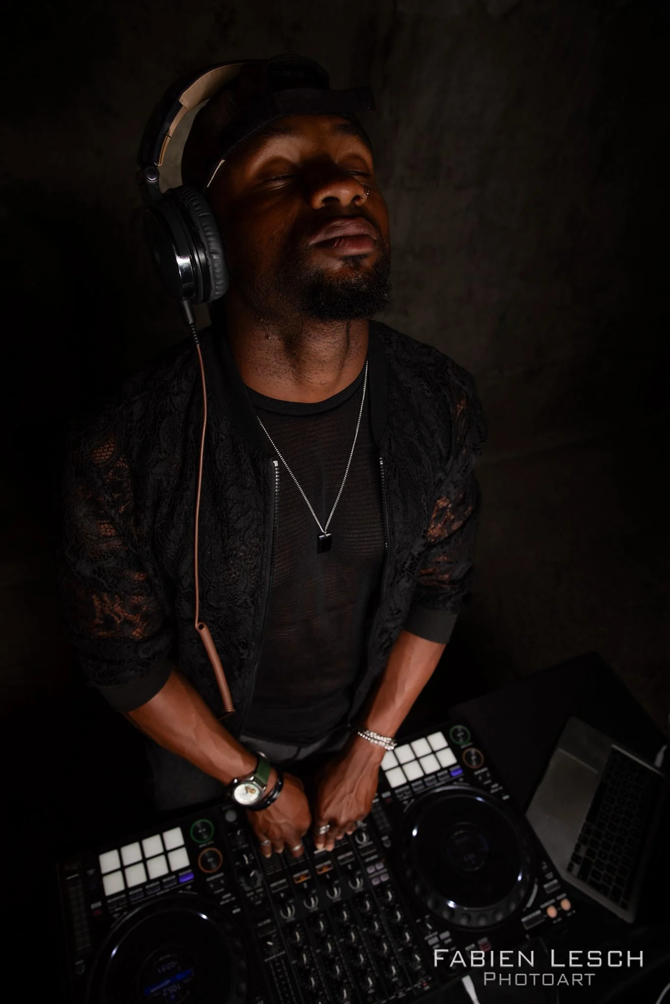 Portrait de DJ, casque sur les oreilles, penché sur son contrôleur en lumière tamisée