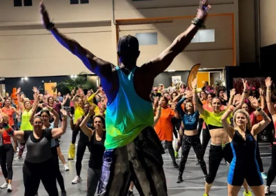 Cours de Zumba collectif dans une grande salle, participants en tenue fluo suivant l'animateur