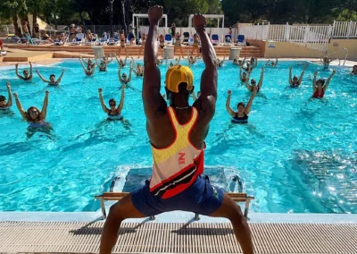 Séance d'aqua-zumba animée au bord d'une piscine extérieure, participants dans l'eau bras levés