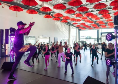 Animateur de Zumba sur scène face à un large public, sous un plafond de parapluies rouges
